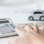 hand using calculator with cash and a toy car