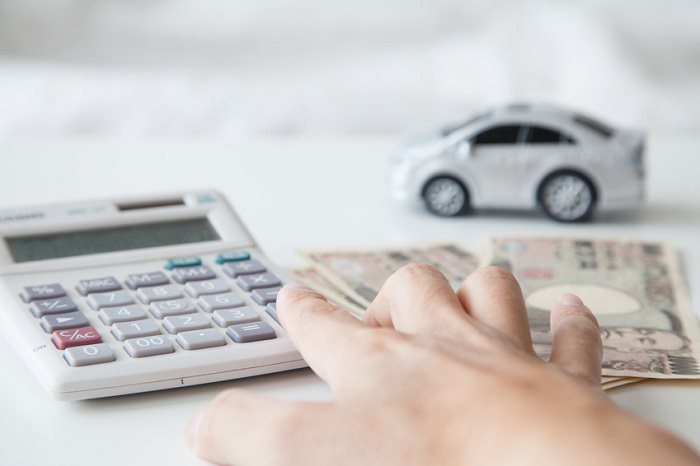 hand using calculator with cash and a toy car